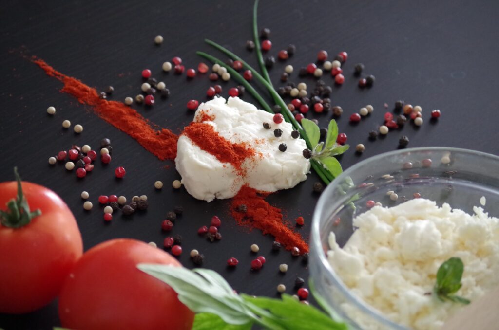 Kajmak topped with Hungarian paprika and pepper, surrounded by tomatoes and another bowl of kajmak spread.