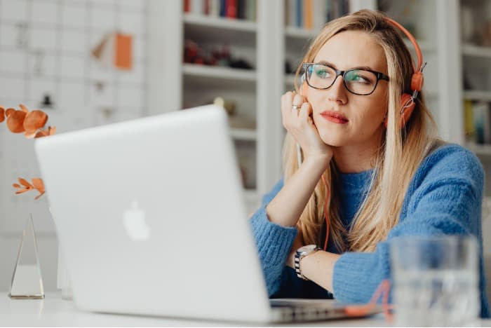 A girl with glasses in deep thoughts, sitting at a laptop and listening to music using headphones