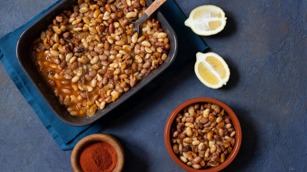 A bowl of baked beans, two lemon slices, and spices laying on a table