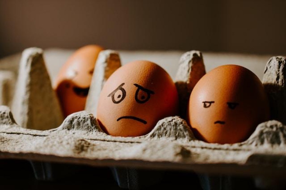 Eggs with drawn faces in a cardboard container. The central egg has a sad face.