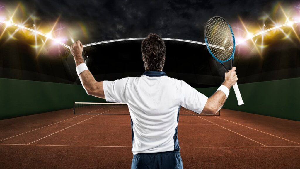 A man in a white T-shirt, on the tennis court holding a tennis racquet