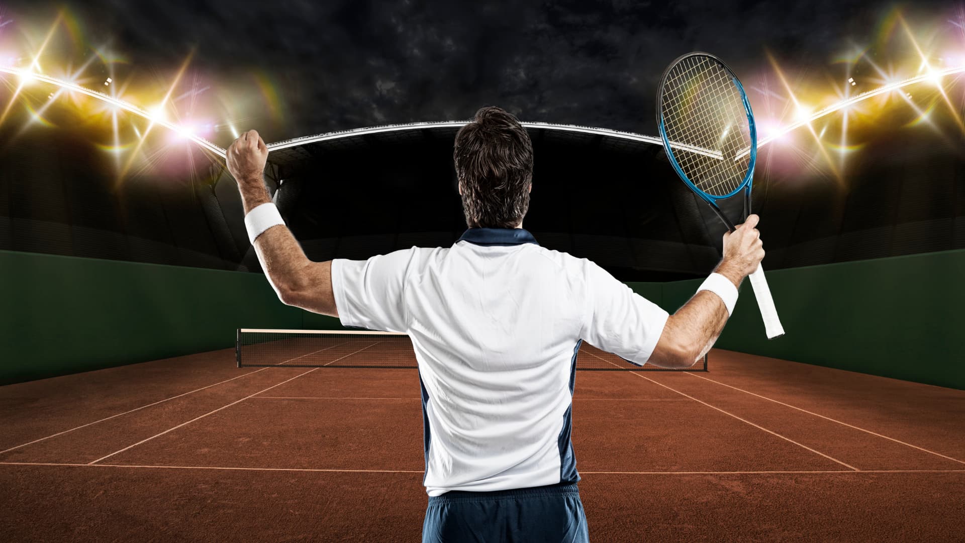 A man in a white T-shirt, on the tennis court holding a tennis racquet