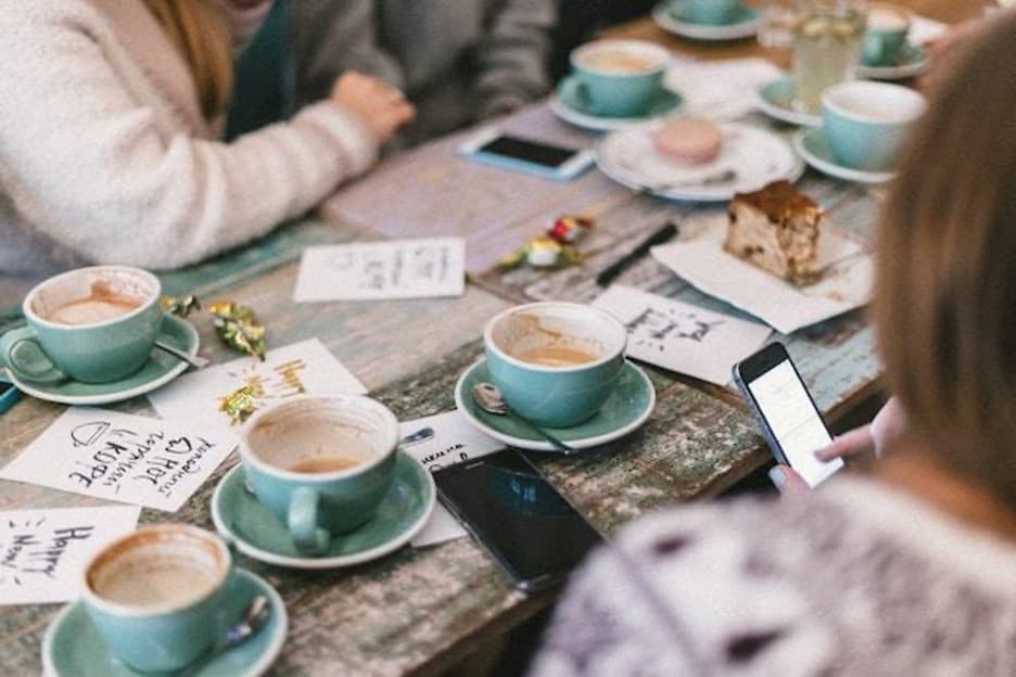A wooden table full of empty cups of coffee, surrounded by people.