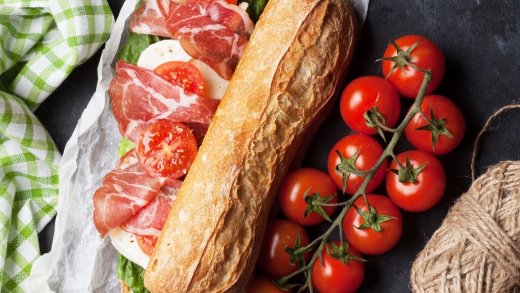 A sandwich with lettuce, tomato, and meat, on a black plate.
