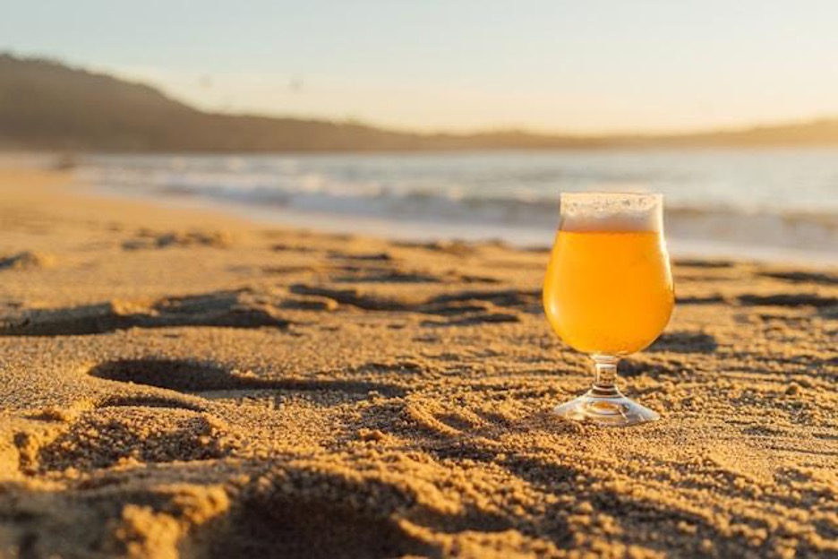 A glass of beer on a sandy beach.