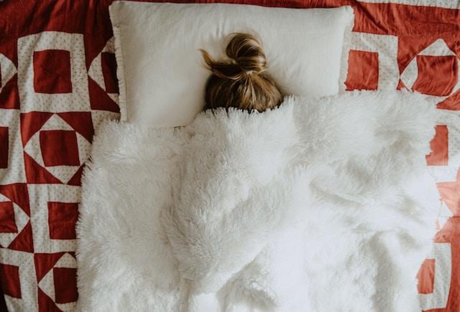 A woman in a bad, with her face and body covered by a white blanket.