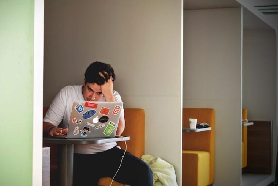 A man looking at a laptop, holding his head in his hand.