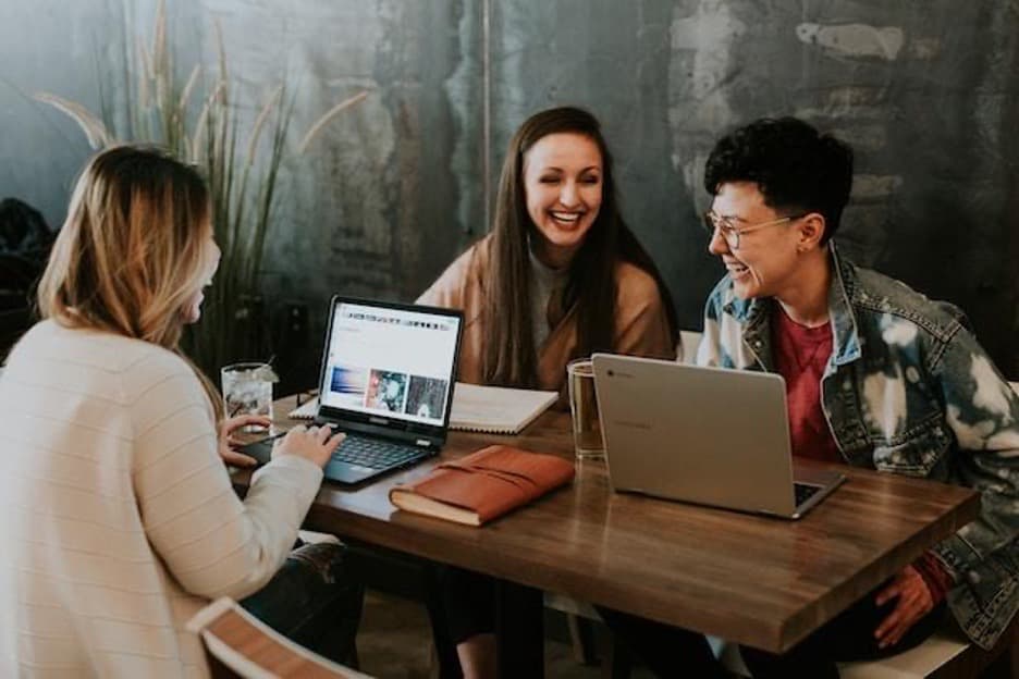 Three young people at a desk, working on laptops and smiling.