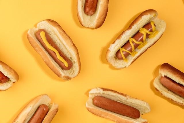 Seven hot dogs in front of a yellow background.