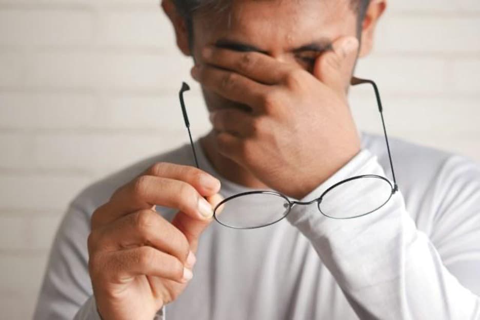 A man with one hand on his eyes and holding eyeglasses with the other.