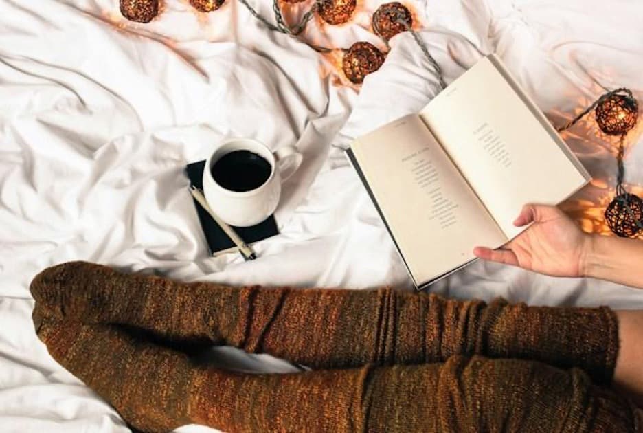 Legs in brown stockings, a book, and a mug of coffee.