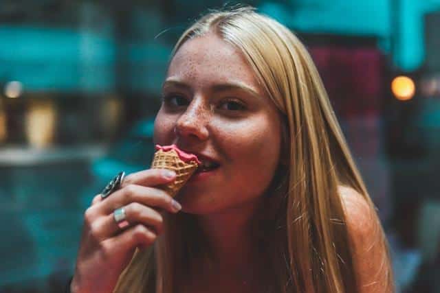 A woman eating a pink ice cream in a cone