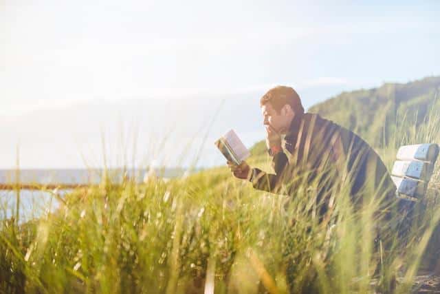 A man studying Serbian on a bench by a lake.
