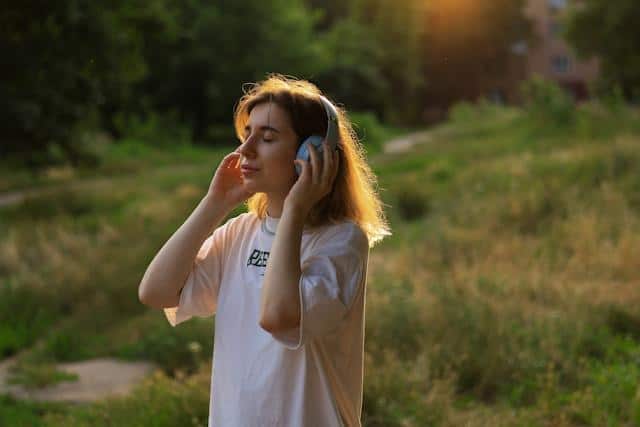 A woman with headphones, walking in a park, listening to a podcast, trying to learn Serbian quickly.