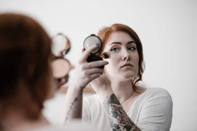 A woman holding a mirror and putting on makeup.