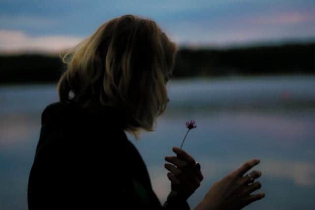 A woman holding a flower playing the he loves me, he loves me not game.