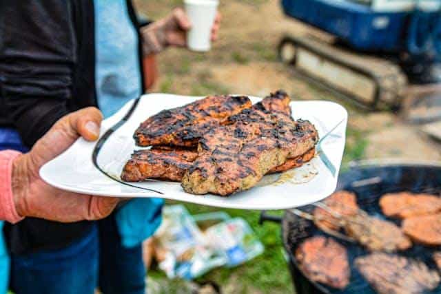 Person holding a plate of grilled meat