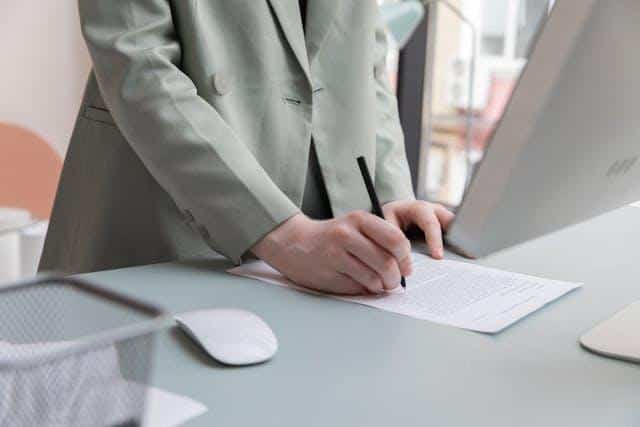 A woman in a suit at a desk handling paperwork.
